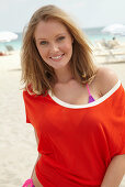 A young blonde woman on a beach wearing a purple bikini and an orange top