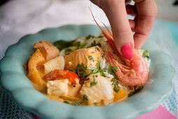 A woman garnishing moqueca (Brazilian fish stew) with prawns