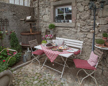 Set table with chairs and bench next to vintage wine press on cobbled terrace