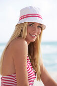 A young blonde woman on a beach wearing a red-and-white striped top and a white hat