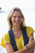 Junge blonde Frau mit gelbem Shirt und Jeansweste im Strand