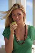 A young blonde woman with an apple on a beach wearing a green top
