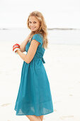 A young blonde woman on a beach wearing a blue summer dress