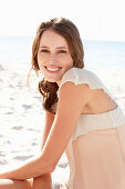 A young brunette woman on a beach wearing a beige top