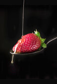 Close-up shot of fresh ripe red strawberry in flowing honey syrup