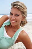 A mature blonde woman on a beach wearing a white top and a turquoise vest