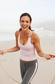 Junge brünette Frau im Sportoutfit und mit Sprungseil am Strand