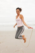 A young brunette woman on a beach wearing a sports outfit with a skipping rope