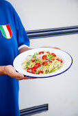 Frau serviert Teller Spaghetti mit Pesto und Kirschtomaten