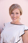 Blonde Frau in heller Bluse mit schwarzer Bordüre vor rosa Hintergrund Studio Shot