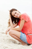 A brunette woman on a beach wearing a salmon-coloured top and a denim skirt