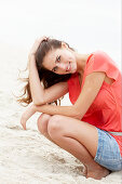 Brünette Frau in lachsfarbenem Top und Jeansrock am Strand