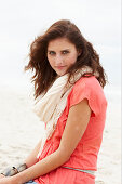 A brunette woman on a beach wearing a scarf and a salmon-coloured top