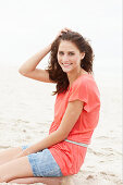 A brunette woman on a beach wearing a salmon-coloured top and a denim skirt