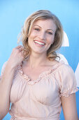 A blonde woman standing against a blue surface wearing a pink short-sleeved blouse