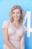 A blonde woman standing against a blue surface wearing a pink short-sleeved blouse