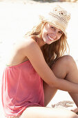 A young blonde woman on a beach wearing a pink top and a beige hat