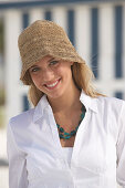 Junge blonde Frau in weißer Bluse und braunem Hut am Strand