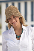 A young blonde woman on a beach wearing a white blouse and a brown hat