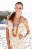 Junge brünette Frau im hellen Sommerkleid und Halskette am Strand