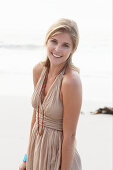 A blonde woman on a beach wearing a beige summer dress