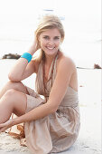 A blonde woman on a beach wearing a beige summer dress