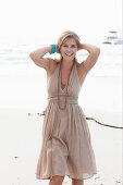 A blonde woman on a beach wearing a beige summer dress