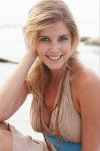 A blonde woman on a beach wearing a beige summer dress