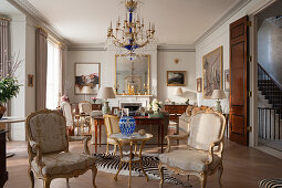 Französische, vergoldete Sessel in elegantem Salon, Kronleuchter aus geschliffenem Glas und Teppich aus Zebrafell-Imitat