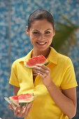 A young brunette woman wearing a yellow polo shirt and holding a slice of watermelon