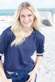 A young blonde woman on a beach wearing a long-sleeved blue shirt