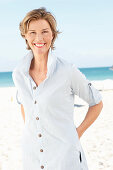 Reife Frau mit blonder Kurzhaarfrisur in hellblau gestreiftem Hemd am Strand