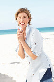 A mature woman with short blonde hair on a beach wearing a light-blue striped short and blue jeans