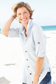 Reife Frau mit blonder Kurzhaarfrisur in hellblau gestreiftem Hemd am Strand