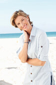 A mature woman with short blonde hair on a beach wearing a light-blue striped short