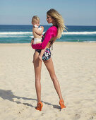 A young woman wearing a colourful bikini and a pink bolero holding a baby