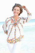 A mature woman by the sea wearing a printed tunic blouse
