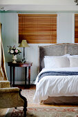 Doppelbett mit Betthaupt und runder Beistelltisch vor Fenster im Schlafzimmer