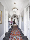 Long hallway with round arches, light gray wall, white doors and carpet runner