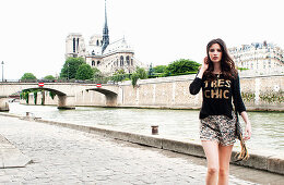 A young brunette woman wearing a shirt and a skirt on the bank of the River Seine near Notre-Dame