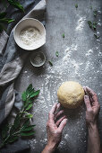Person kneading ball of soft dough on marble counter sprinkled with flour