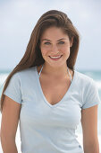 A young brunette woman on a beach wearing a beige top