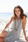 A young brunette woman on a beach wearing a beige summer dress and a necklace