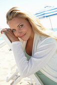 A blonde woman on a beach wearing a turquoise top and a white jacket