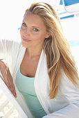 A blonde woman on a beach wearing a turquoise top and a white jacket