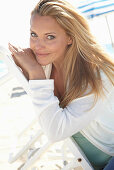 A blonde woman on a beach wearing a turquoise top and a white jacket