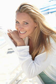 A blonde woman on a beach wearing a turquoise top and a white jacket