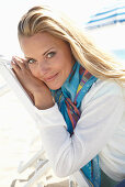 A blonde woman on a beach wearing a colourful scarf and a white jacket