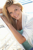 A blonde woman on a beach wearing a turquoise top and a white jacket