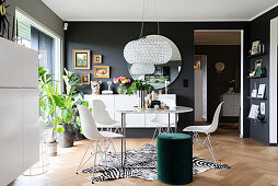 Filigraner Esstisch mit Klassikerstühlen auf Zebrafell, grüner Pouf und weiße Sideboards im Wohnraum mit dunklen Wänden